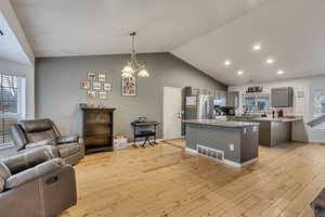 Kitchen with stainless steel refrigerator, gray cabinetry, light hardwood / wood-style floors, decorative light fixtures, and vaulted ceiling