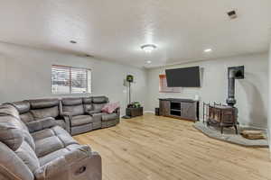 Living room featuring light wood-type flooring, a textured ceiling, and a wood stove