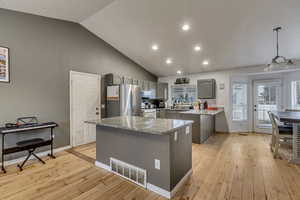 Kitchen featuring gray cabinets, decorative light fixtures, stainless steel fridge, a center island, and light hardwood / wood-style flooring