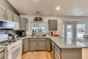 Kitchen with sink, stainless steel appliances, light stone counters, light hardwood / wood-style floors, and kitchen peninsula