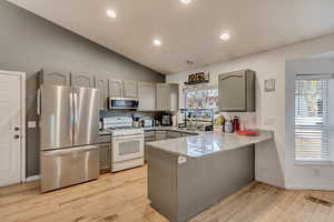 Kitchen with sink, appliances with stainless steel finishes, gray cabinetry, kitchen peninsula, and light wood-type flooring