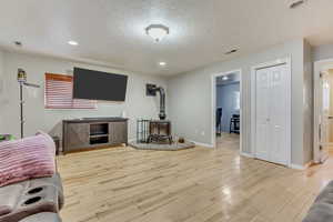 Living room with a wood stove, a textured ceiling, and light hardwood / wood-style floors