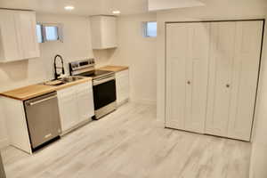 Kitchen with white cabinetry, sink, stainless steel appliances, and light wood-type flooring