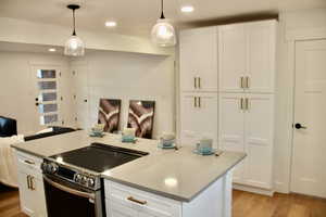 Kitchen with stainless steel electric stove, an island with sink, white cabinets, hanging light fixtures, and light wood-type flooring