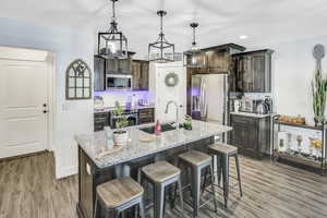 Kitchen with appliances with stainless steel finishes, sink, a center island with sink, and dark brown cabinets