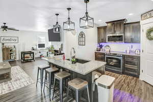 Kitchen with pendant lighting, sink, dark brown cabinetry, stainless steel appliances, and light stone countertops