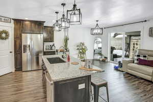 Kitchen with sink, decorative light fixtures, dark brown cabinets, a center island with sink, and stainless steel fridge