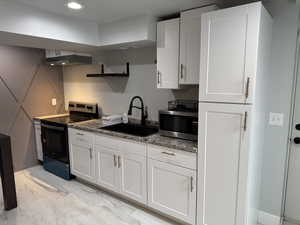 ADU Kitchen featuring sink, dark stone countertops, range hood, stainless steel appliances, and white cabinets