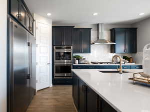 Kitchen featuring wall chimney exhaust hood, sink, dark hardwood / wood-style floors, stainless steel appliances, and decorative backsplash