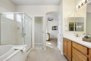 Full bath featuring a stall shower, a garden tub, ceiling fan, vanity, and baseboards
