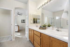Full bath with a ceiling fan, a shower stall, double vanity, tile patterned floors, and baseboards