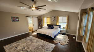 Bedroom with dark hardwood / wood-style floors, vaulted ceiling, a barn door, and ceiling fan