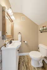 Bathroom with vanity, toilet, vaulted ceiling, and wood-type flooring