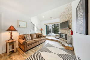 Living room with vaulted ceiling, a large fireplace, light hardwood / wood-style floors, and baseboard heating