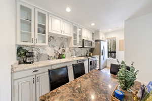 Kitchen with sink, light stone countertops, white cabinets, and appliances with stainless steel finishes