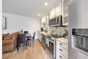 Kitchen featuring appliances with stainless steel finishes, white cabinetry, backsplash, light stone countertops, and light hardwood / wood-style floors