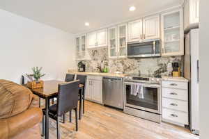 Kitchen with decorative backsplash, stainless steel appliances, light hardwood / wood-style floors, and white cabinets