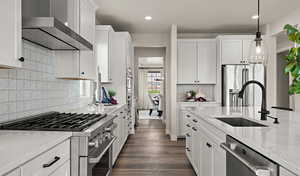 Kitchen featuring sink, white cabinetry, hanging light fixtures, high end appliances, and wall chimney exhaust hood