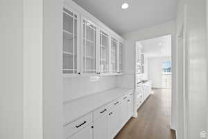 Bar with stainless steel microwave, decorative backsplash, light hardwood / wood-style flooring, and white cabinets