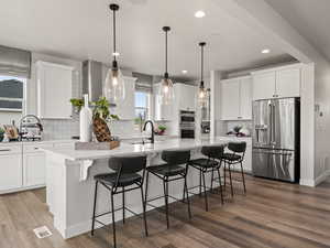 Kitchen featuring sink, appliances with stainless steel finishes, a center island, white cabinets, and decorative light fixtures