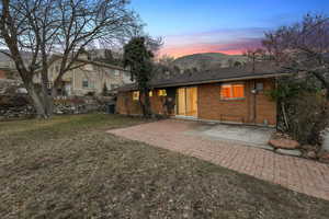 Back house at dusk featuring a mountain view, a lawn, and a patio area