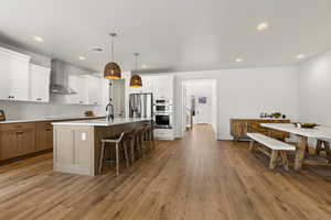 Kitchen with appliances with stainless steel finishes, a center island with sink, white cabinets, and wall chimney exhaust hood