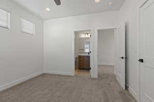 Unfurnished bedroom with ceiling fan, light colored carpet, and ensuite bath