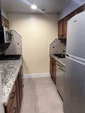 Kitchen with stainless steel appliances, light stone countertops, sink, and light tile patterned floors