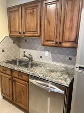 Kitchen with sink, stainless steel dishwasher, light stone counters, and refrigerator