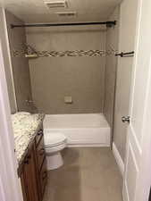 Full bathroom featuring tiled shower / bath, tile patterned flooring, vanity, toilet, and a textured ceiling