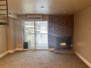 Unfurnished living room featuring a large fireplace, carpet flooring, a wall mounted AC, and a textured ceiling