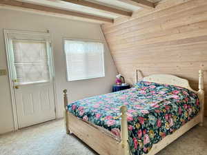 Carpeted bedroom with vaulted ceiling with beams and wooden walls