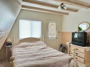 Carpeted bedroom featuring ceiling fan and beamed ceiling