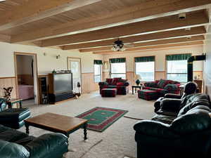 Living room with wooden walls, beamed ceiling, carpet floors, ceiling fan, and wooden ceiling