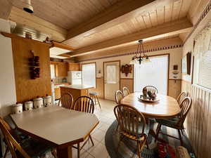 Tiled dining area featuring beamed ceiling, wood ceiling, wooden walls, and a notable chandelier