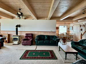 Carpeted living room with wood ceiling, wooden walls, beam ceiling, and a wood stove