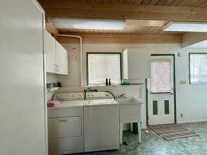 Laundry room featuring wood ceiling, washer and clothes dryer, and cabinets