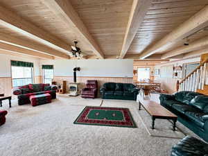 Carpeted living room with plenty of natural light, beamed ceiling, and a wood stove