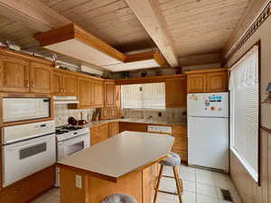 Kitchen with sink, a breakfast bar area, tasteful backsplash, a center island, and white appliances