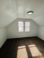 Bonus room with vaulted ceiling, dark carpet, and a textured ceiling