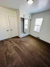 Unfurnished bedroom featuring a textured ceiling, dark carpet, and a closet