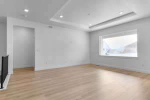 Empty room featuring light wood finished floors, visible vents, a tray ceiling, and a textured ceiling
