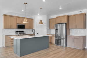 Kitchen featuring light countertops, light wood-style floors, a center island with sink, appliances with stainless steel finishes, and a sink