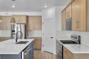 Kitchen with appliances with stainless steel finishes, sink, a kitchen island with sink, and decorative light fixtures