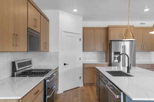 Kitchen with appliances with stainless steel finishes, light wood-type flooring, visible vents, decorative backsplash, and a sink