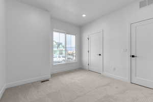 Unfurnished bedroom with recessed lighting, visible vents, light colored carpet, and baseboards