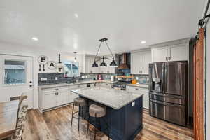 Kitchen featuring wall chimney range hood, sink, stainless steel appliances, a kitchen island, and decorative light fixtures