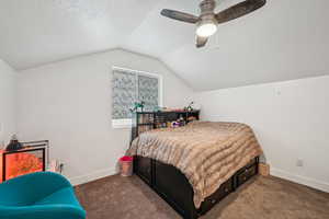 Bedroom featuring ceiling fan, vaulted ceiling, a textured ceiling, and dark colored carpet