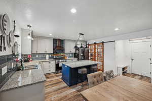 Kitchen featuring pendant lighting, wall chimney range hood, stainless steel range with gas stovetop, a center island, and a barn door