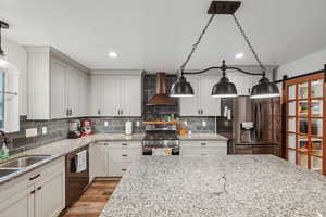 Kitchen with sink, light stone counters, stainless steel appliances, a barn door, and wall chimney exhaust hood